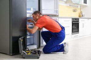 Male-Technician-With-Screwdriver-Repairing-Refrigerator-in-Kitchen-1024x680